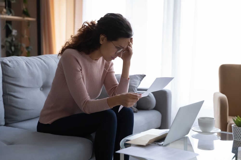 Woman Holding Her Head Reading Denied Insurance Claim Documents